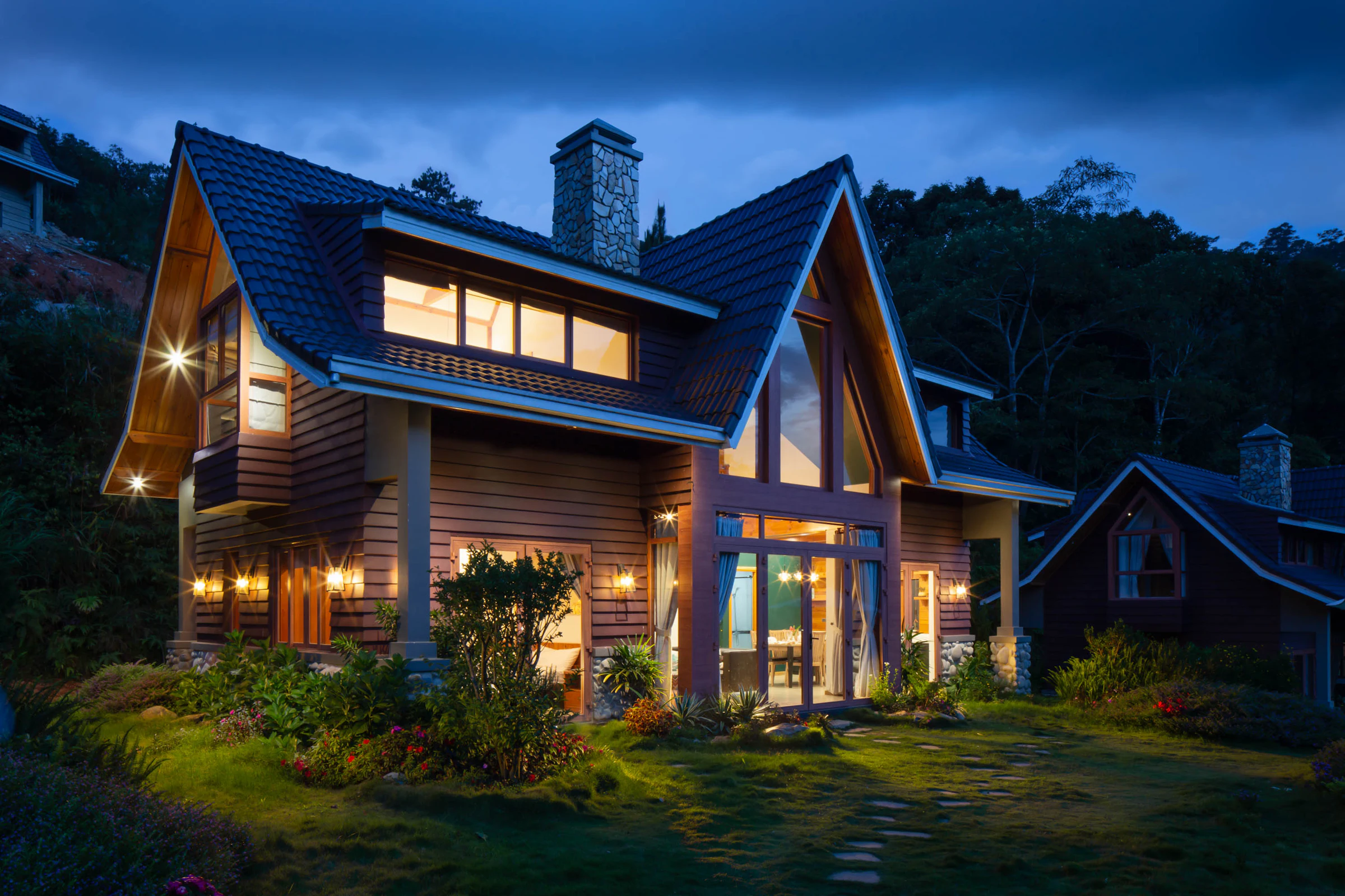 A house at dusk with warm light in the windows and landscaped grounds. Illustrative photography.