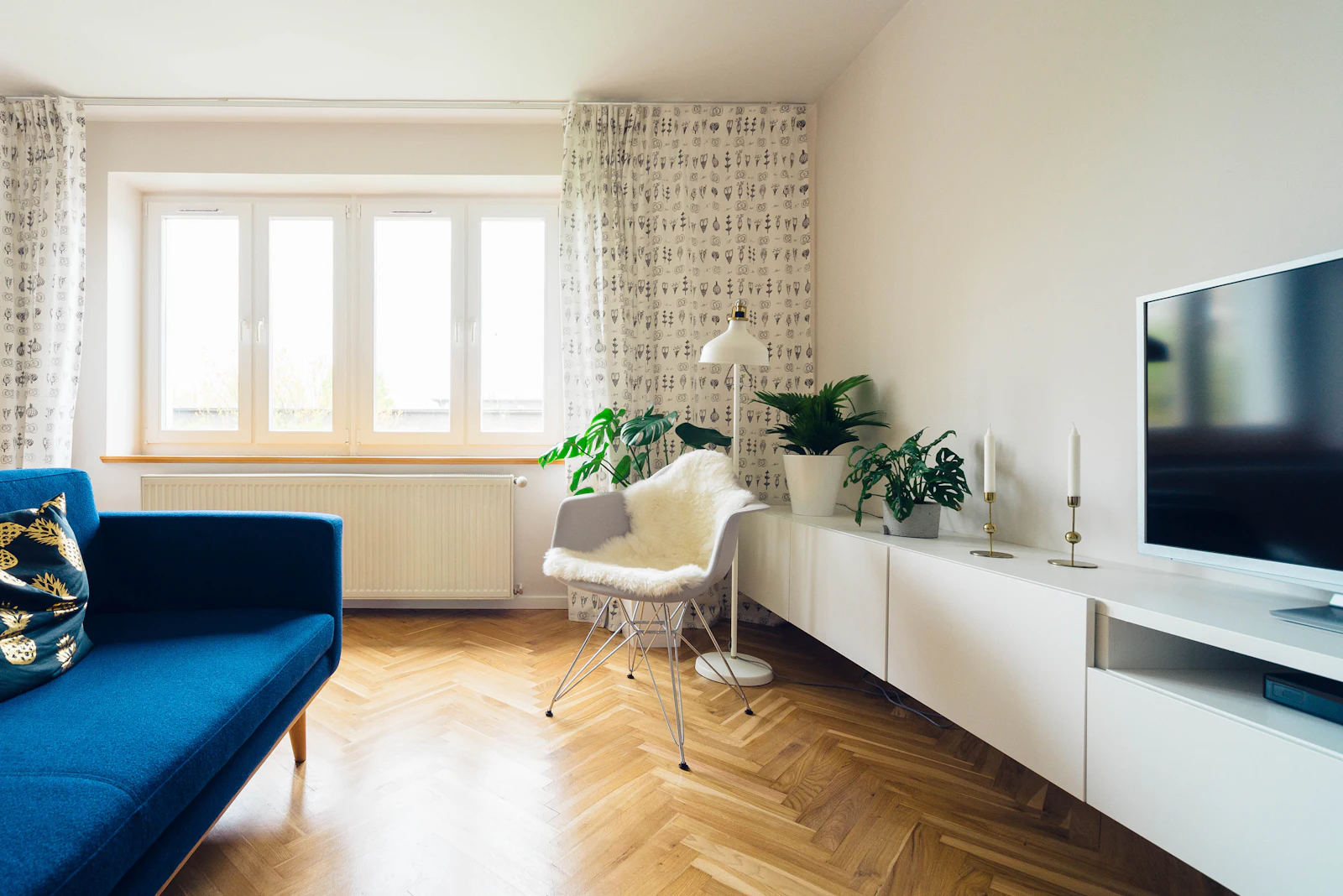 A living room with herringbone floors and a blue sofa beneath tall windows. Illustrative photography.